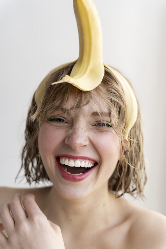 A person rubbing a banana peel on their teeth while smiling, bright bathroom background, close-up focus on white teeth